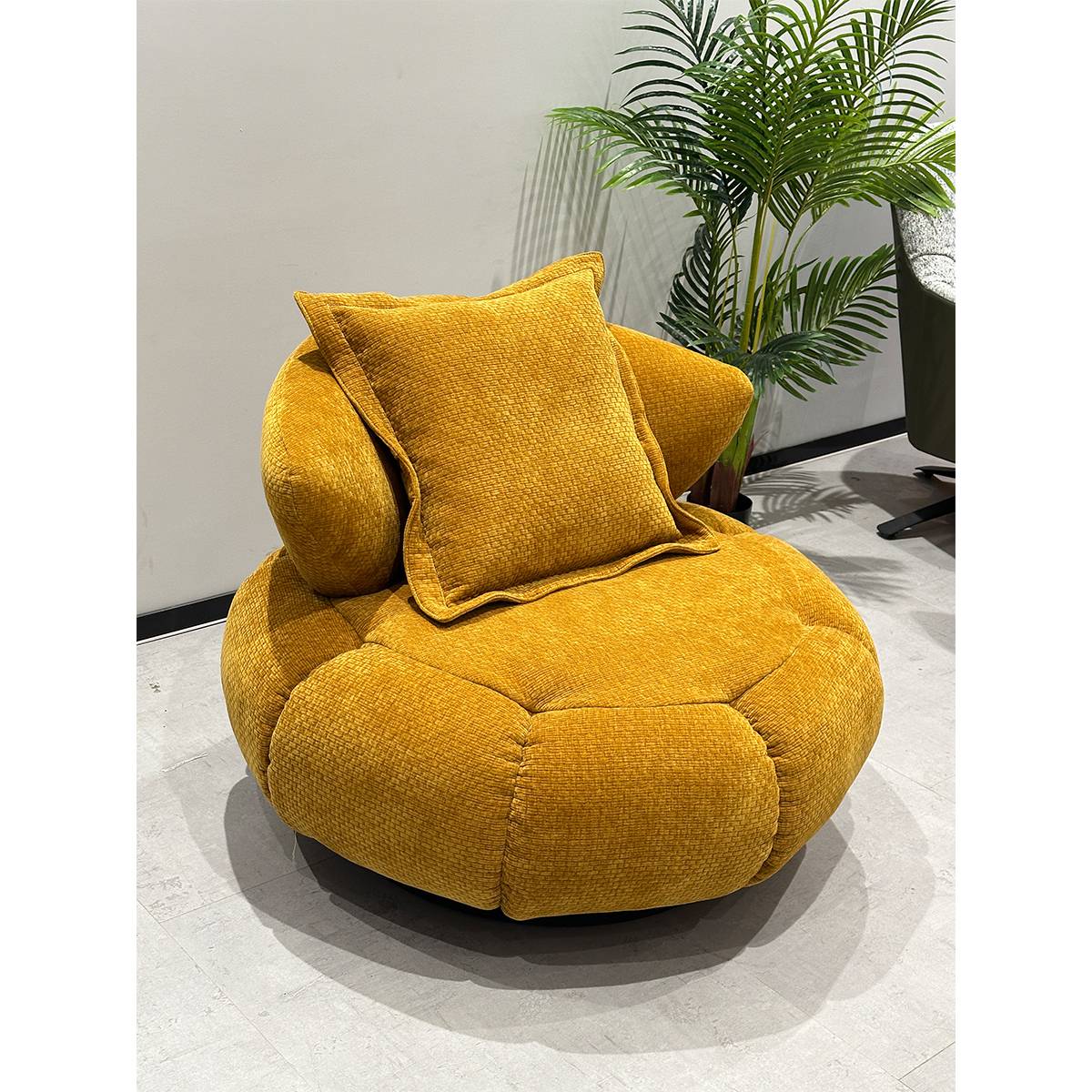 Side angle view of the yellow lounge chair showing the texture of the fabric and the swivel mechanism.