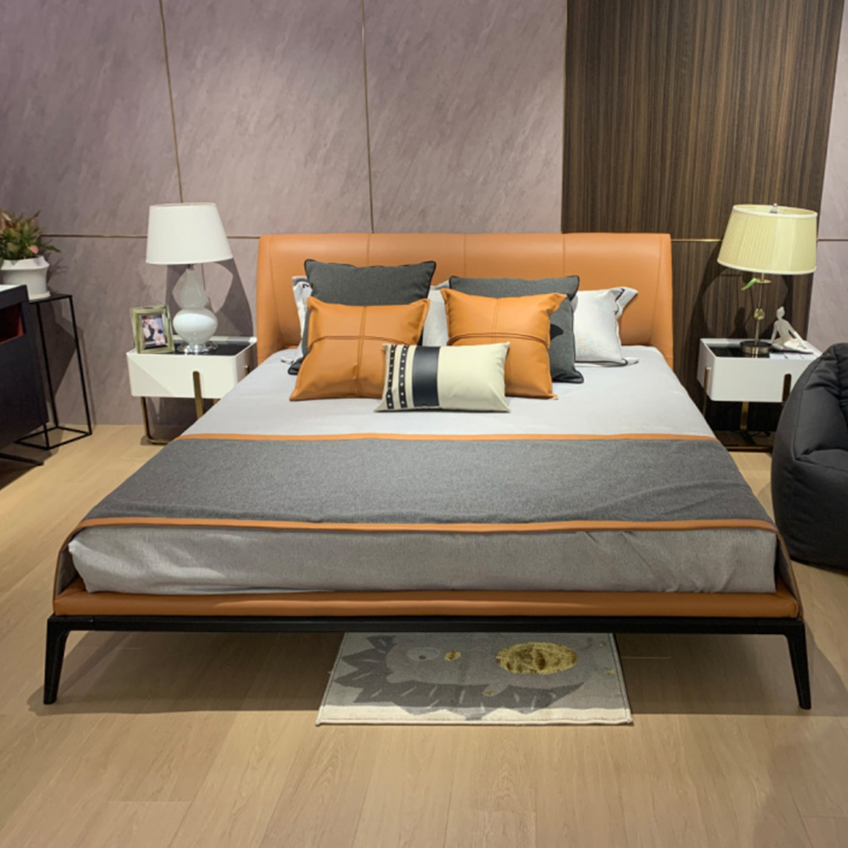 Tan leather bed styled in a bedroom setting with orange and grey pillows