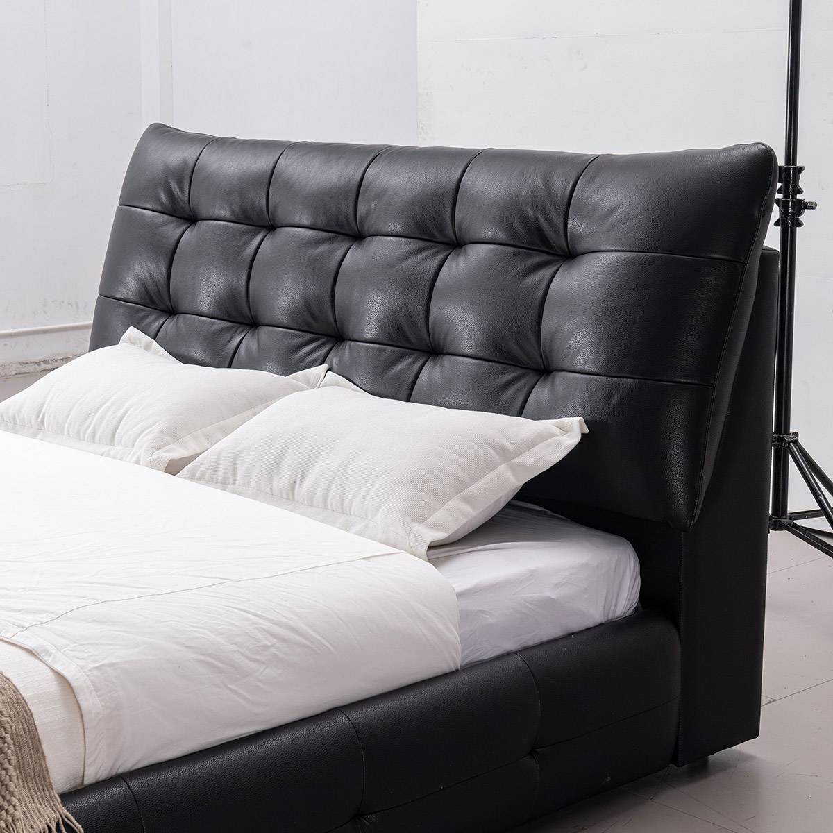 Side angle view of the black leather tufted bed with white bedding