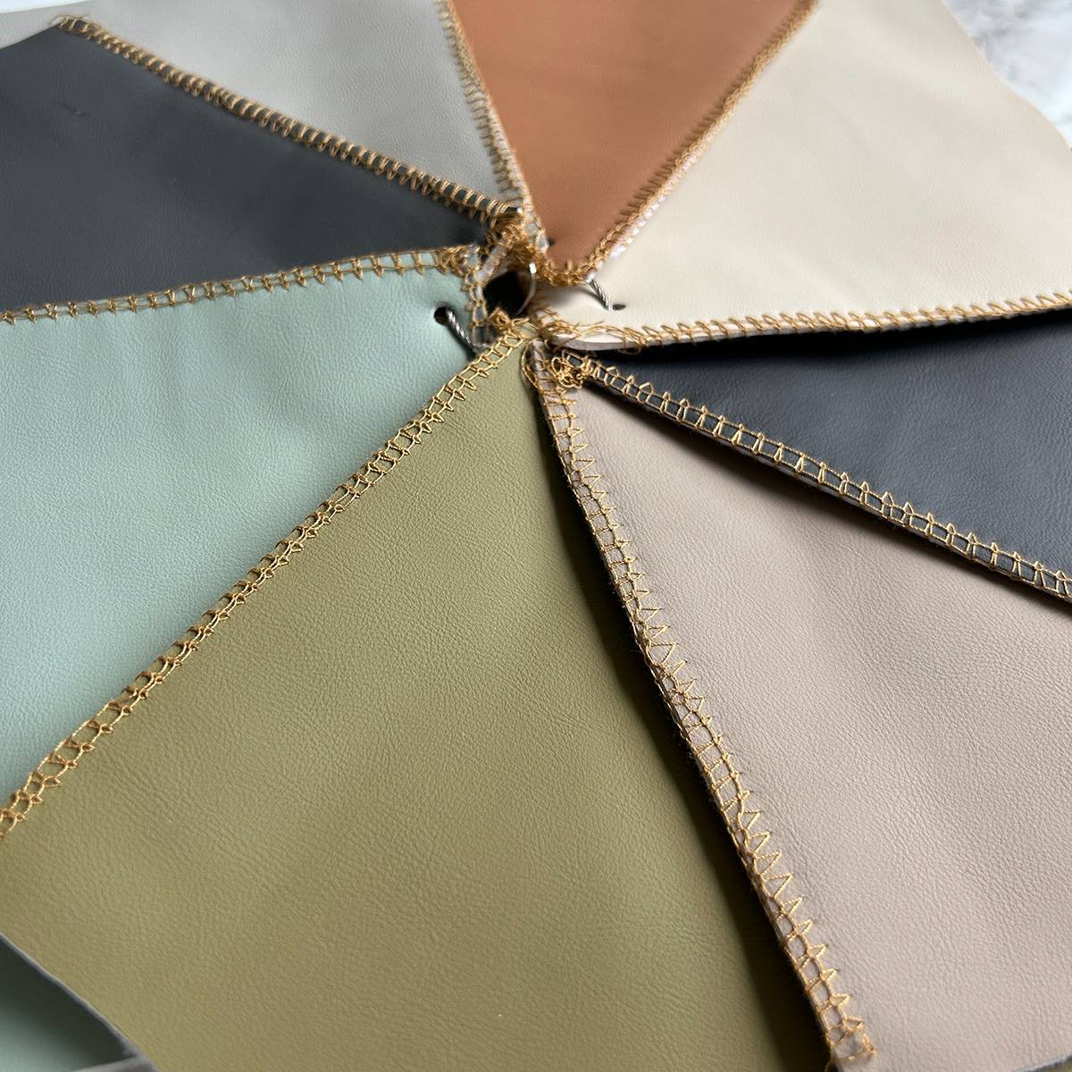 Close-up of leather swatches in mint green, olive, grey, and beige with gold stitching