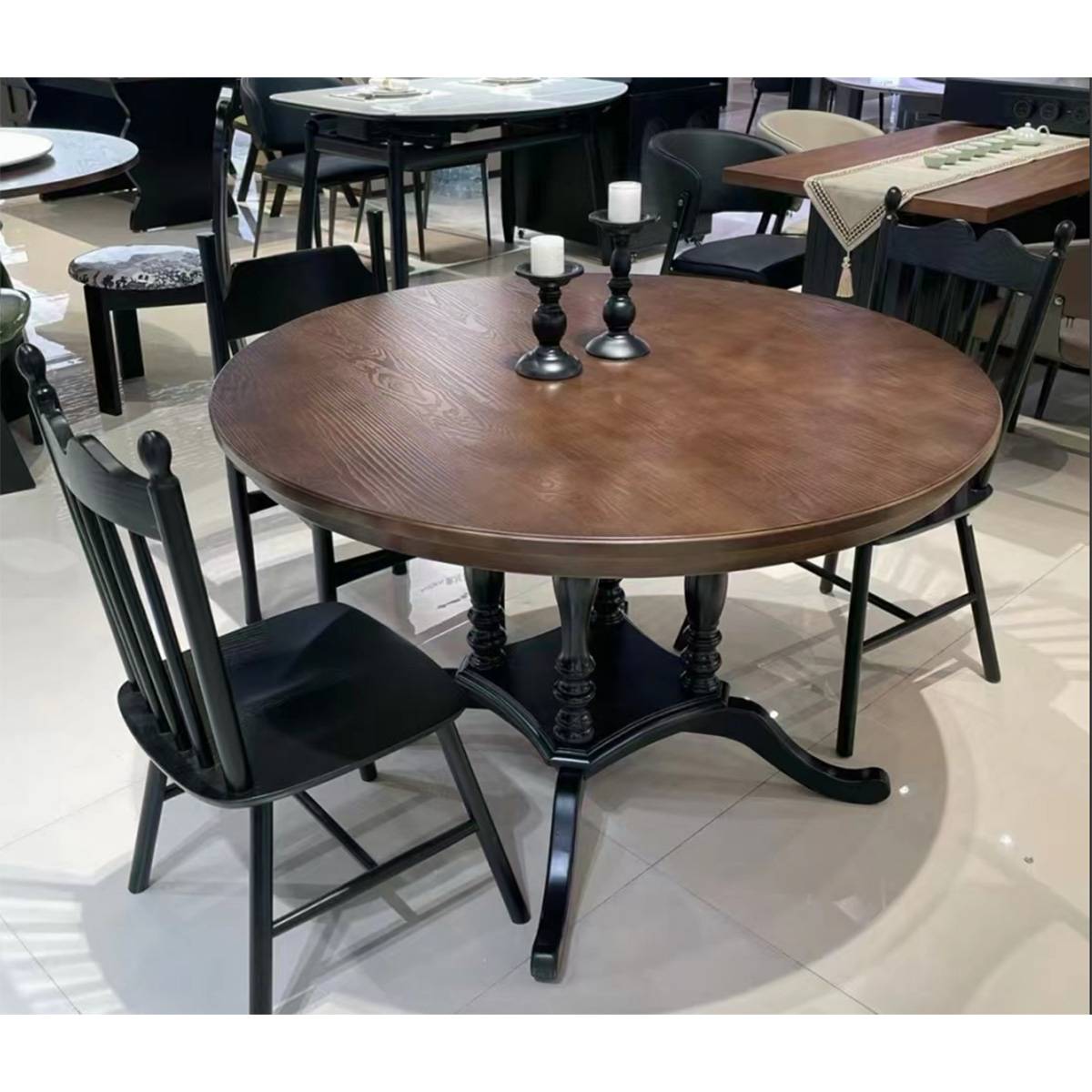 Walnut round dining table with black chairs in a showroom setting