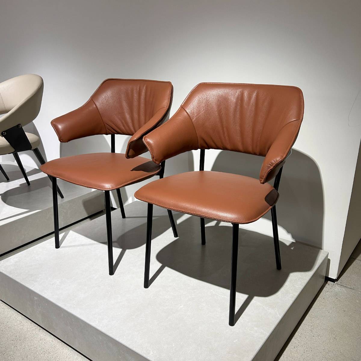 Two brown leather dining chairs displayed on a platform
