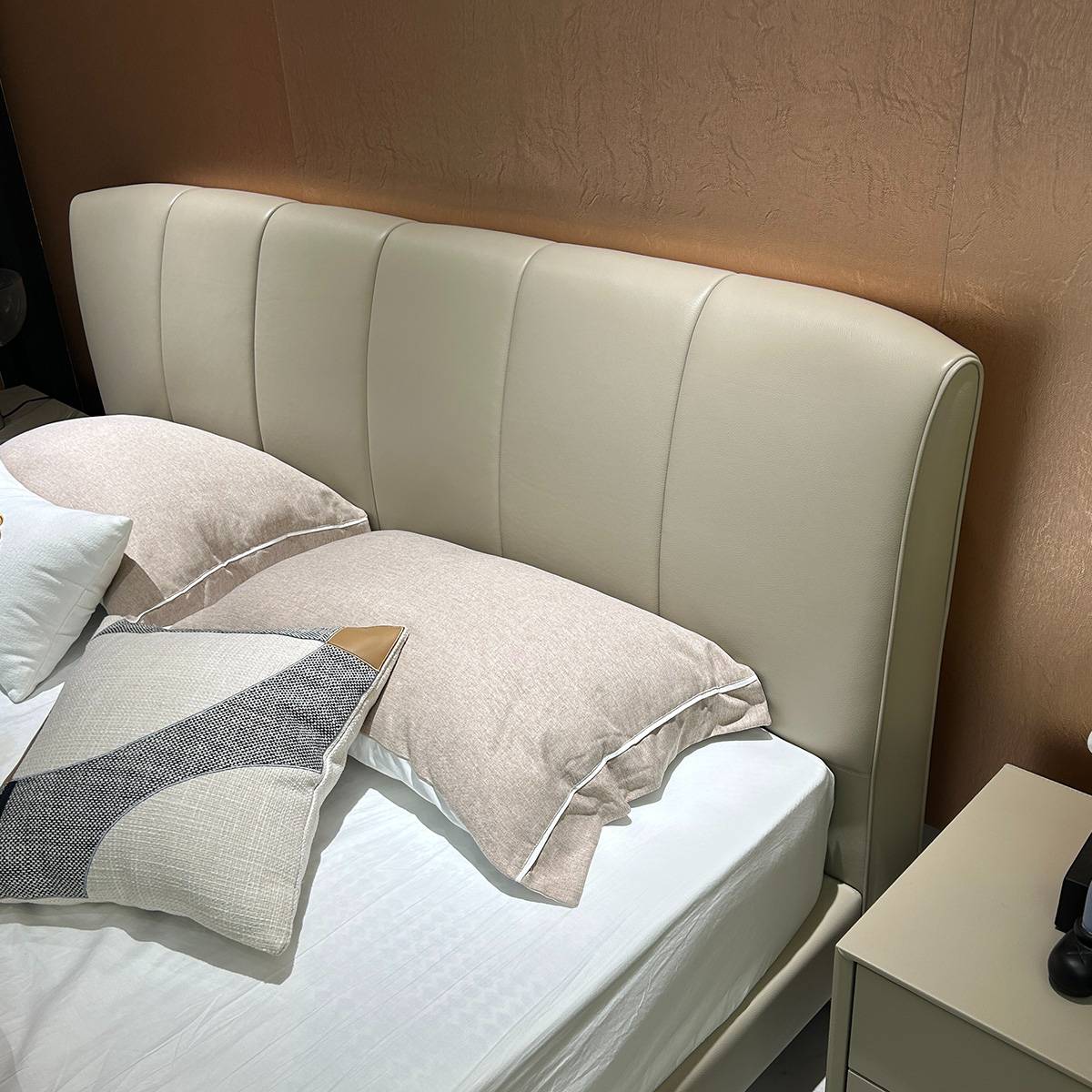 Close-up view of a beige leather bed headboard with vertical tufting and pillows