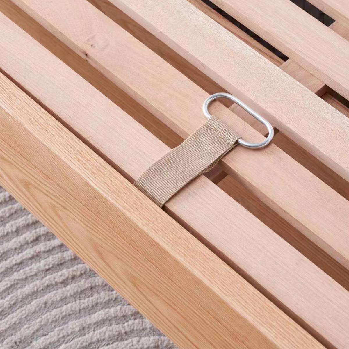 Close-up of the wooden slat bed frame showing the fabric strap and metal D-ring attachment detail.
