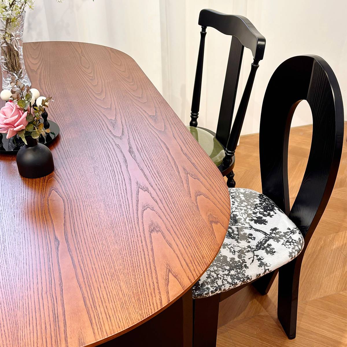 Close-up view of the walnut wood grain on the blade-shaped dining table surface with black chairs.