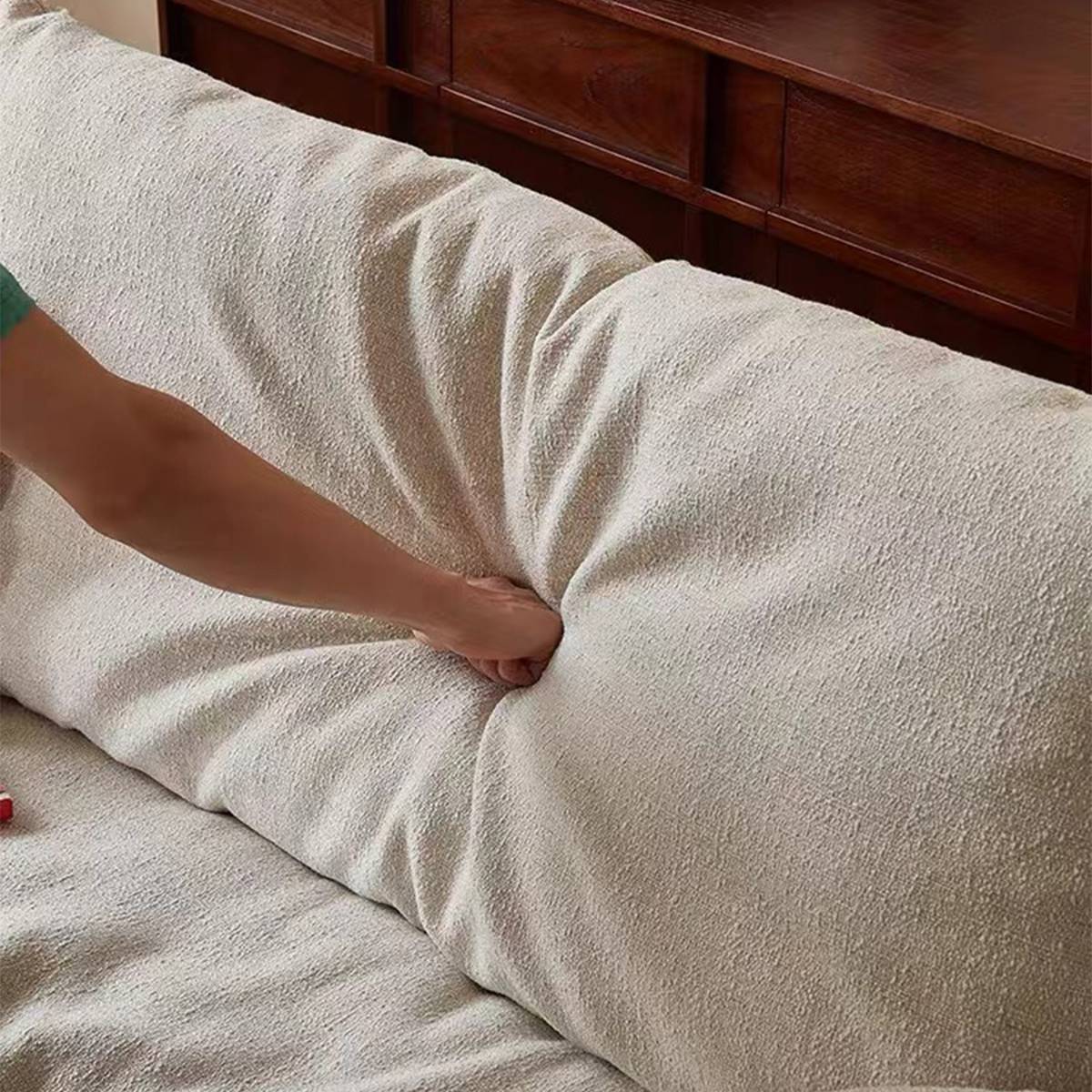 Close-up of a hand pressing into the back cushion of a beige linen sofa to demonstrate softness