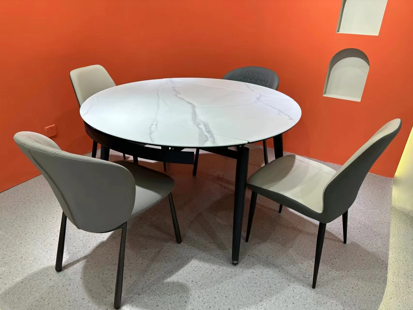 White microcrystalline stone dining table with black steel legs and grey chairs against an orange wall