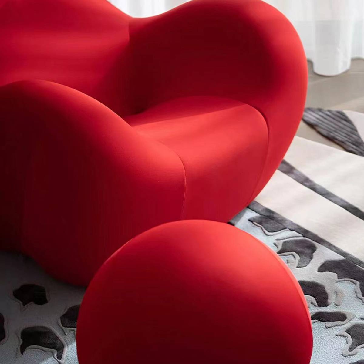 Close-up of a red, organic-shaped lounge chair with a matching ottoman on a patterned rug