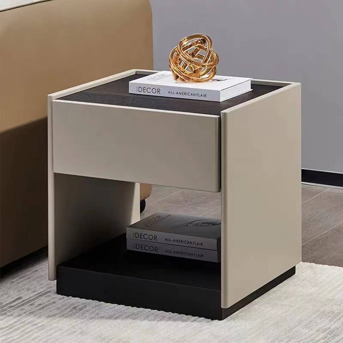 Side view of bedside table next to a bed with books and a gold sculpture on top