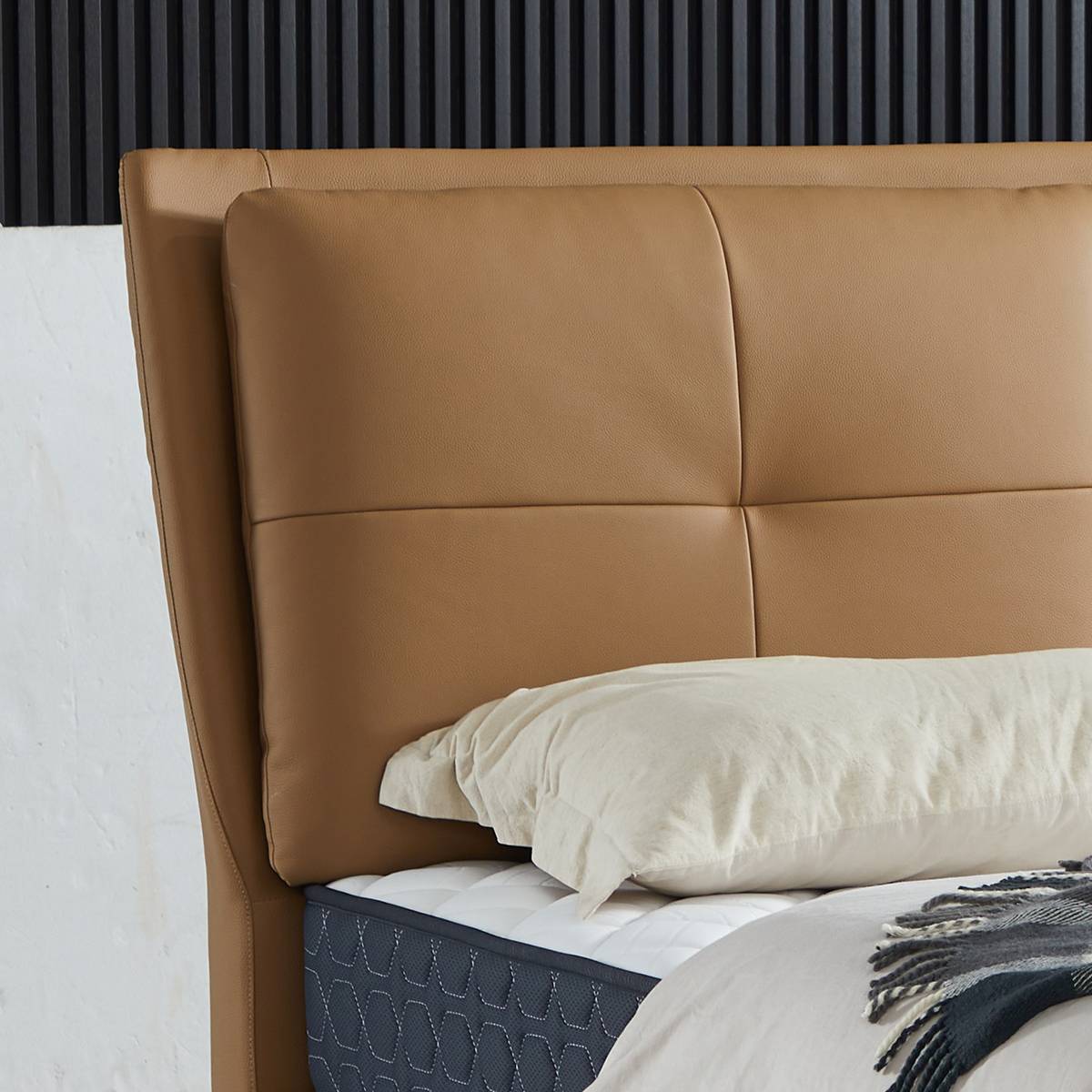 Close-up of a tan leather bed headboard with a quilted mattress and white pillow