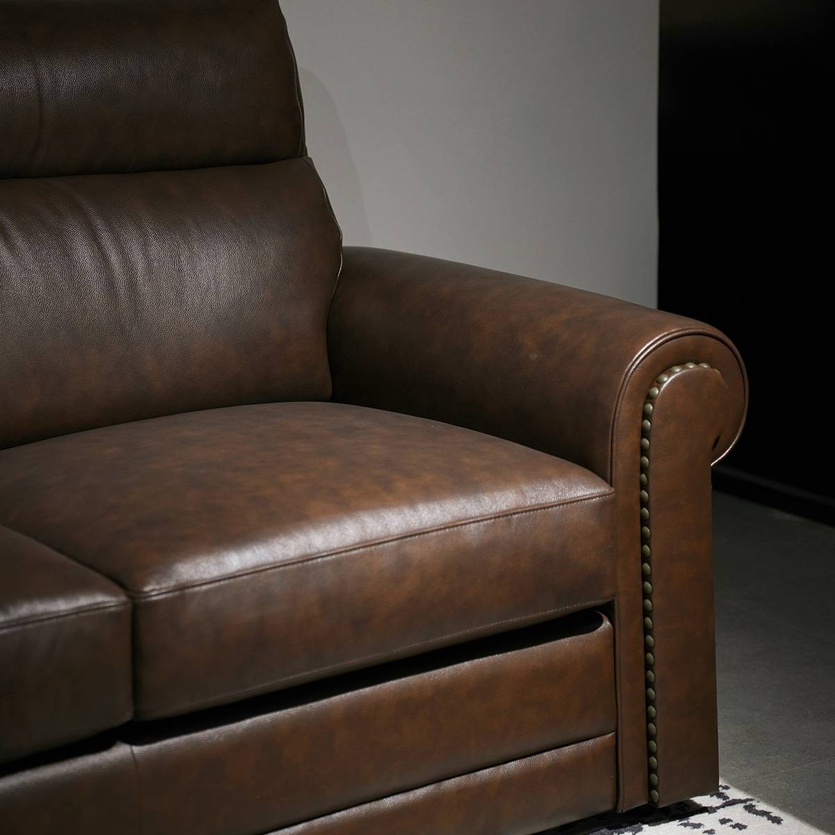 Close-up detail of the sofa armrest showing leather texture and nailhead trim