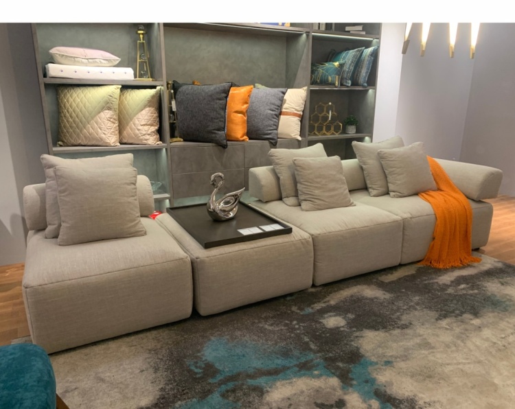 Full view of the sofa in a showroom setting with an orange throw blanket