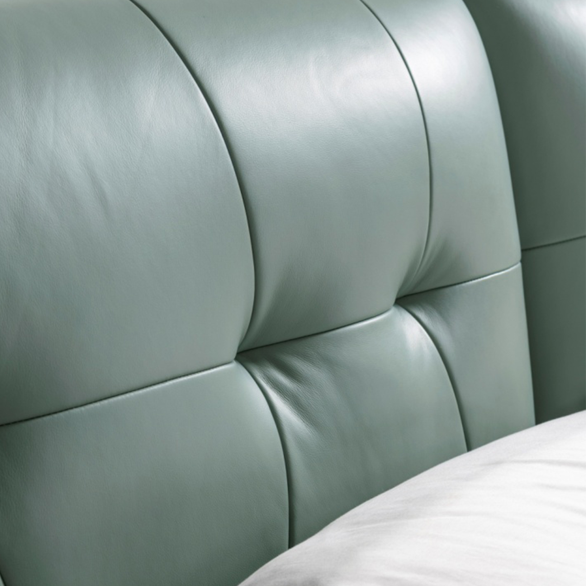 Full view of a sage green leather bed with a tufted headboard and white bedding.