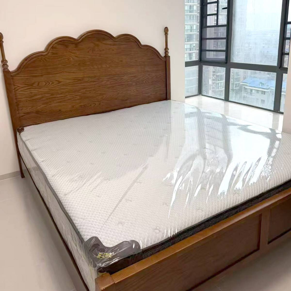 Close-up of the bed frame with a mattress wrapped in plastic, showing the wood grain and construction details