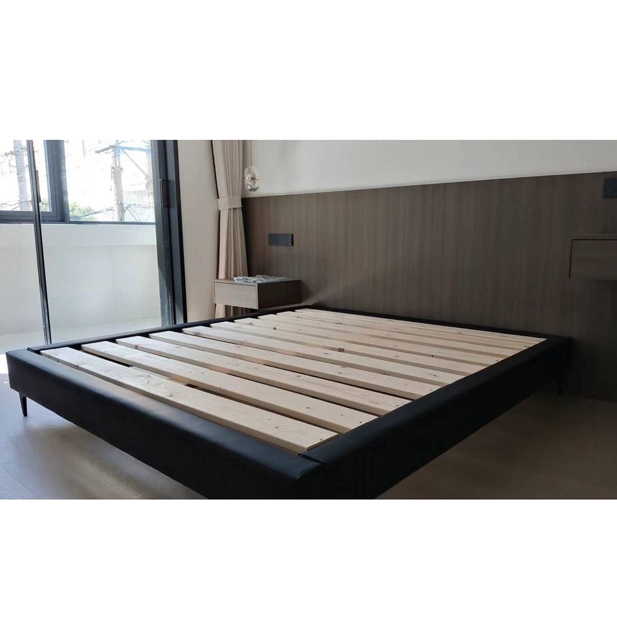 Black upholstered backless bed frame with light wood slats in a modern bedroom setting