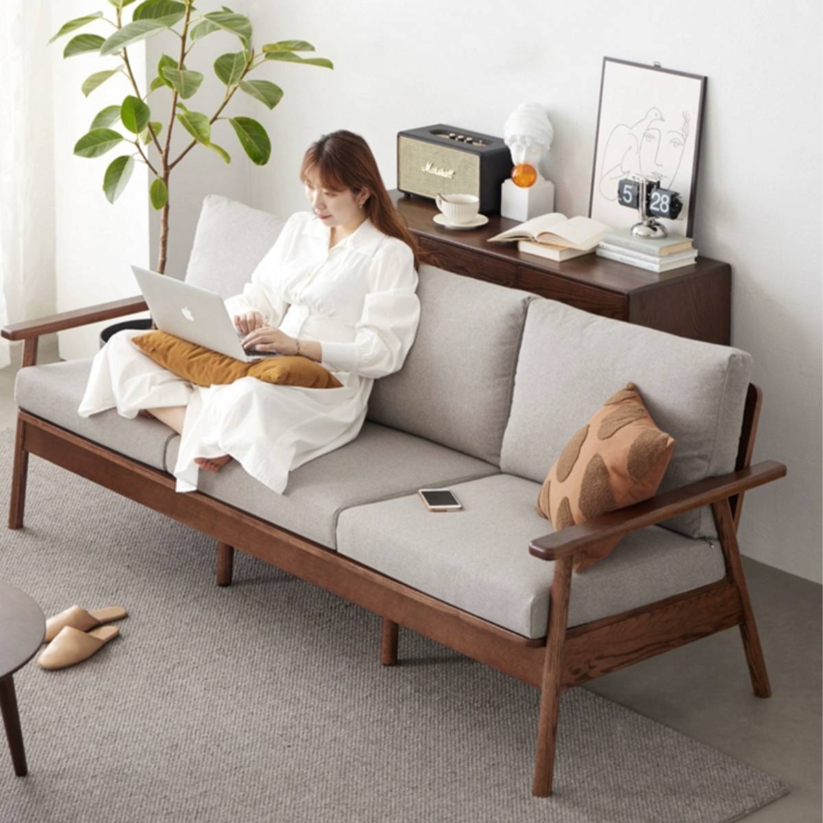 Lifestyle shot of a woman using a laptop on the sofa with grey cushions