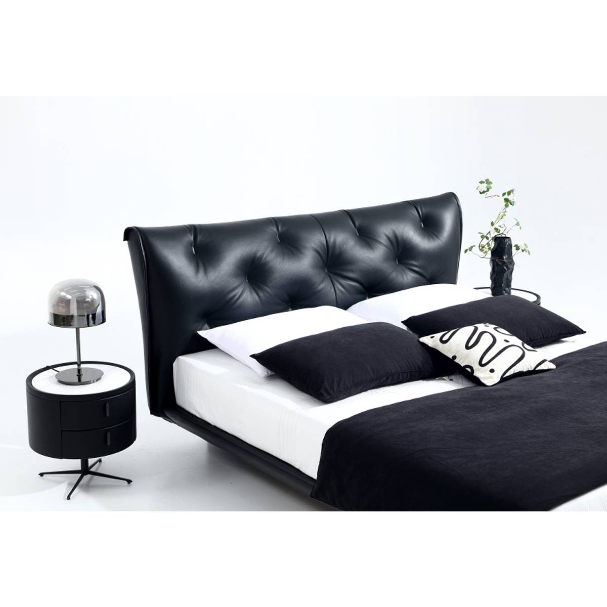 Front view of the black leather bed with white bedding and a bedside table