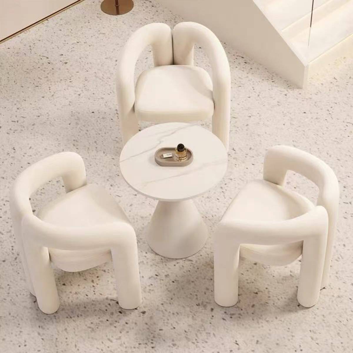Three white lounge chairs with curved frames arranged around a round side table