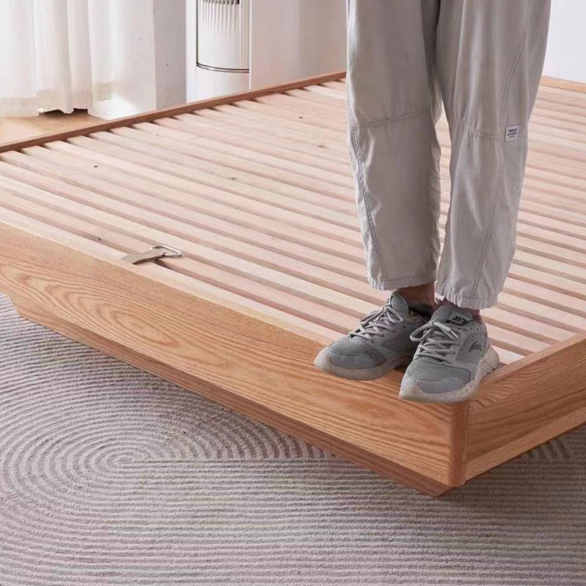 Person standing on the solid wood bed frame to demonstrate the sturdiness of the slatted base.