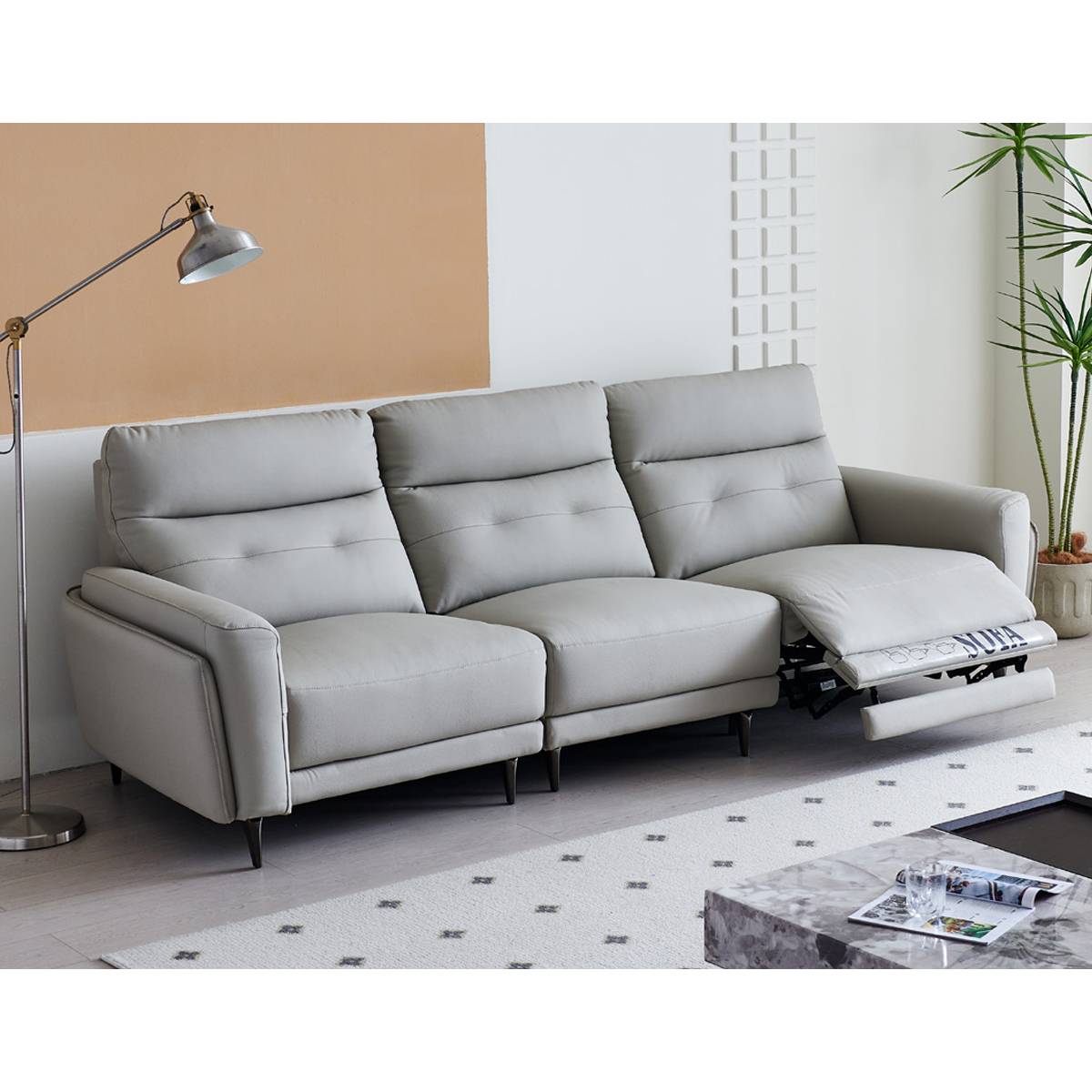 Side view of a light grey leather functional sofa with a woman sitting on it holding a glass