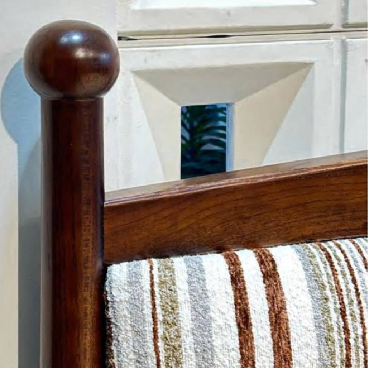 Close-up detail of the wooden bed post and striped fabric headboard