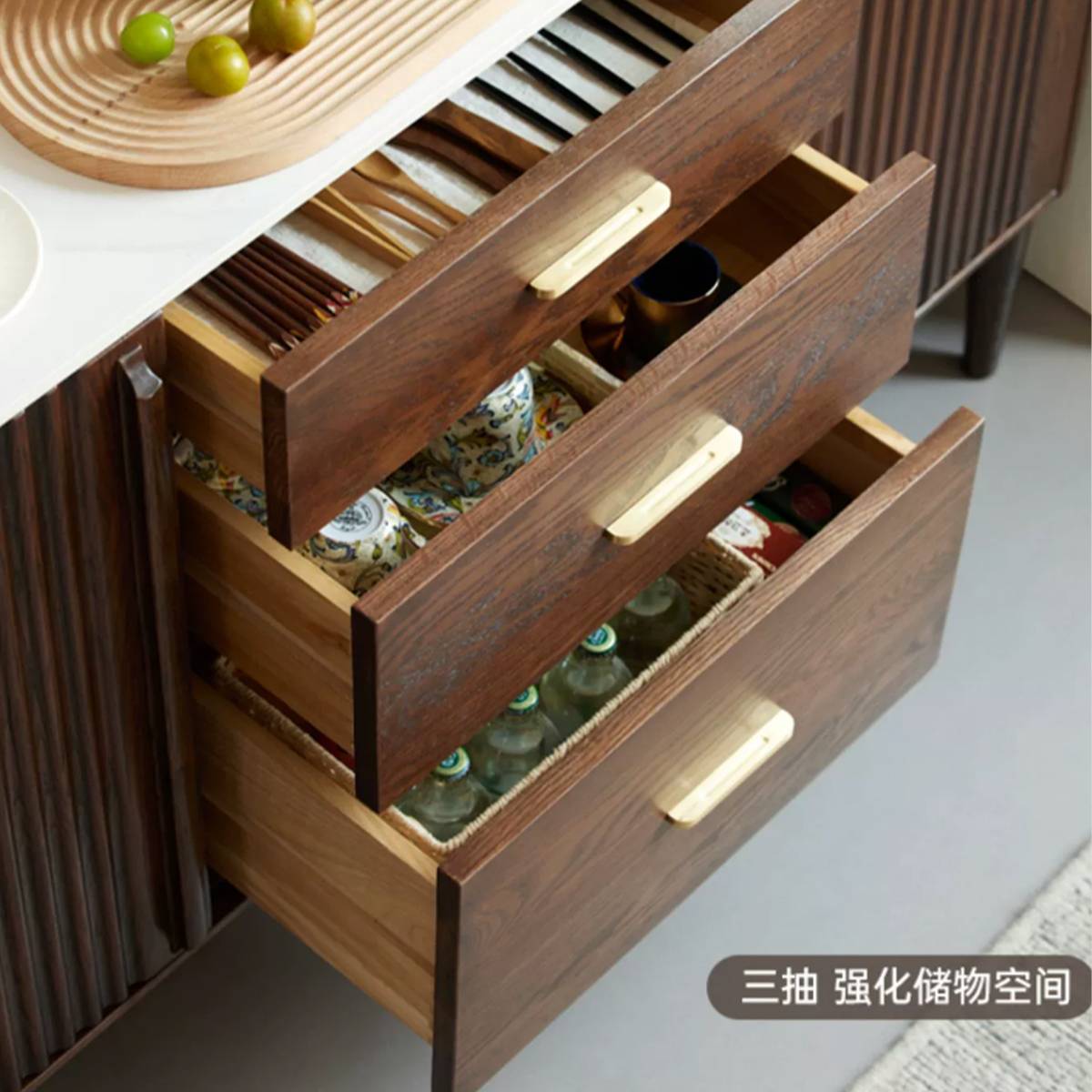 Close-up of the sideboard drawers open, revealing storage for cutlery, cups, and bottles.