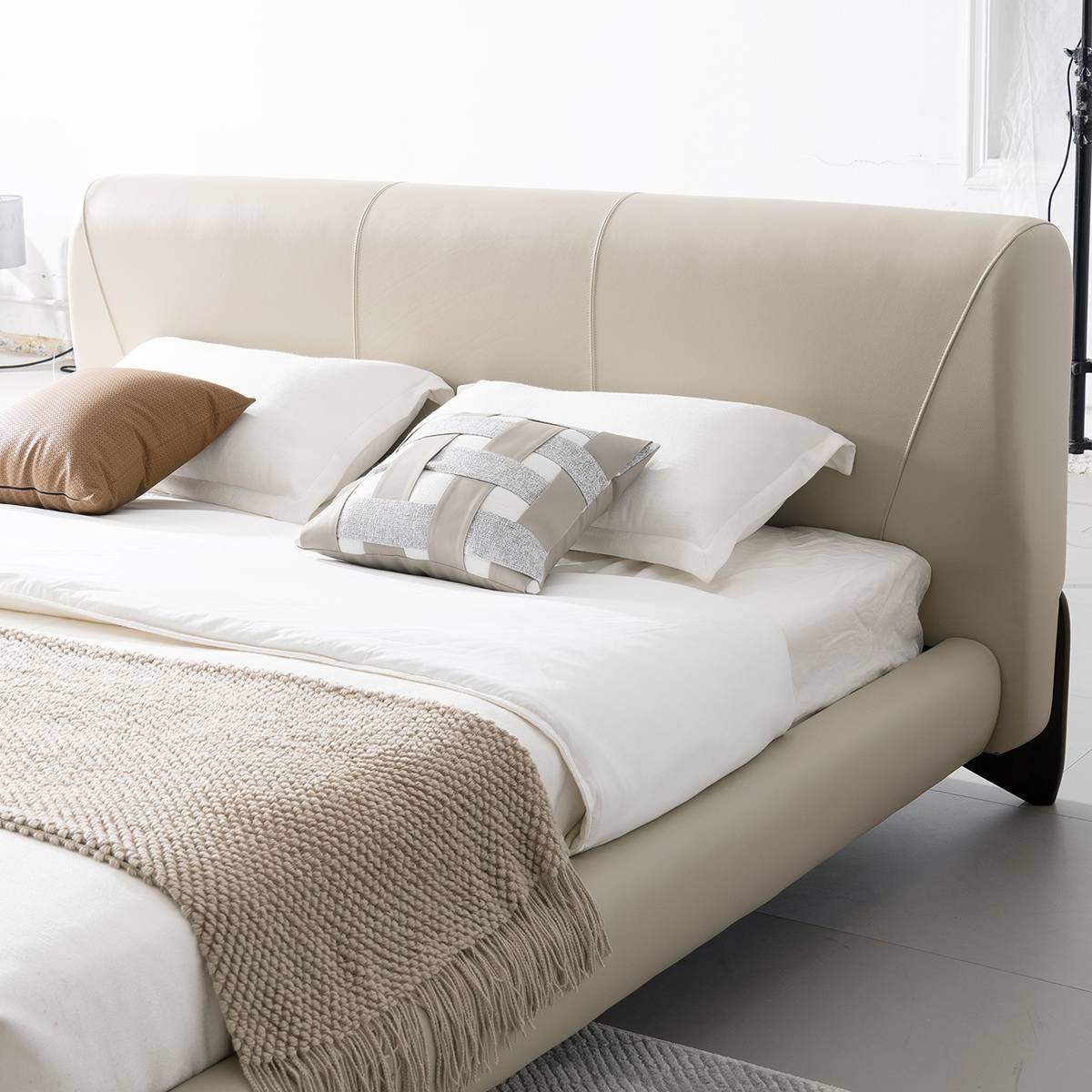 Side view of the beige leather bed with white bedding and a textured throw blanket
