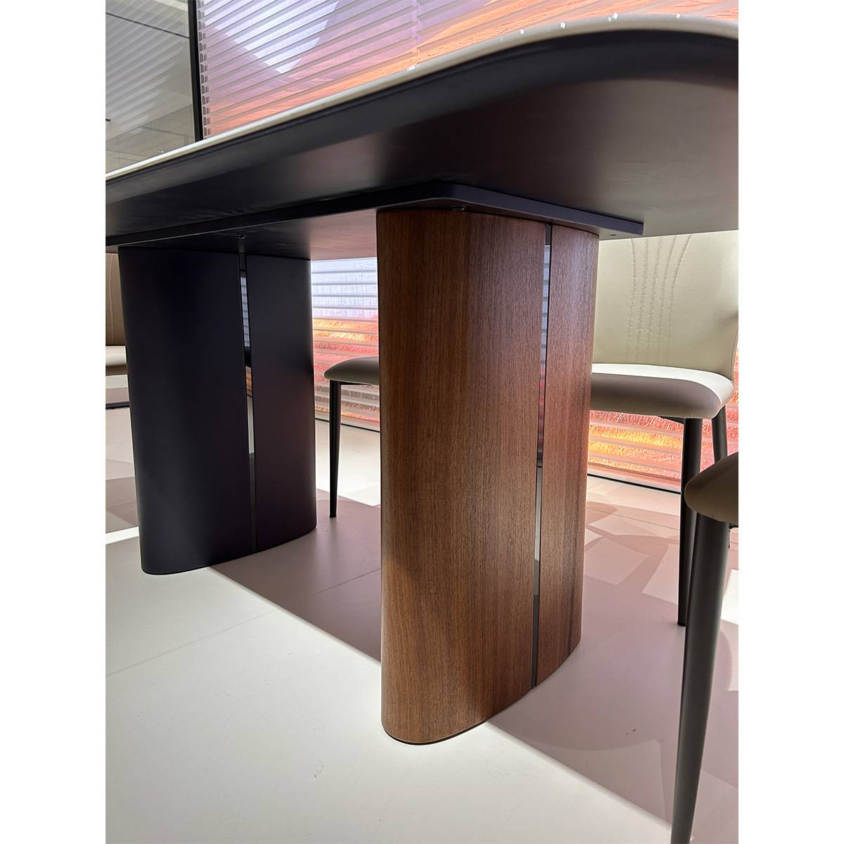 Close-up view of the dining table base showing the curved black and walnut veneer legs supporting the stone top.