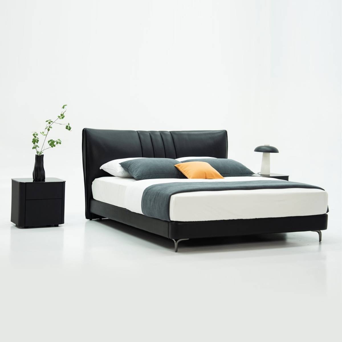 Full view of the black leather bed with grey and orange pillows