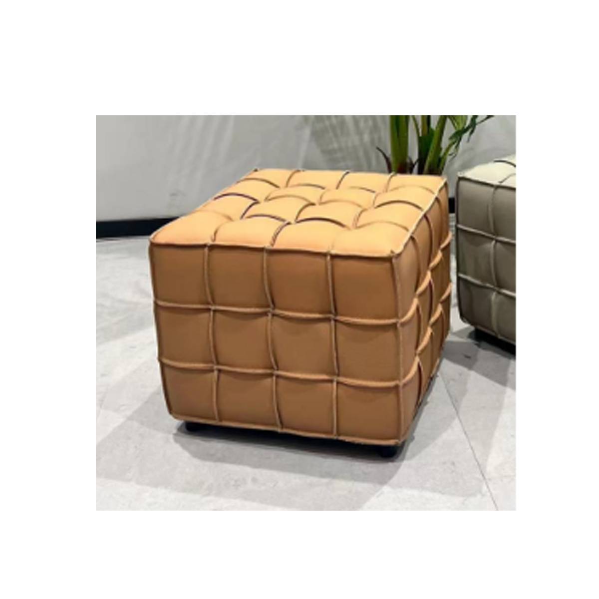 Close-up view of the tan leather cube ottoman showing the woven texture and tufted top surface.