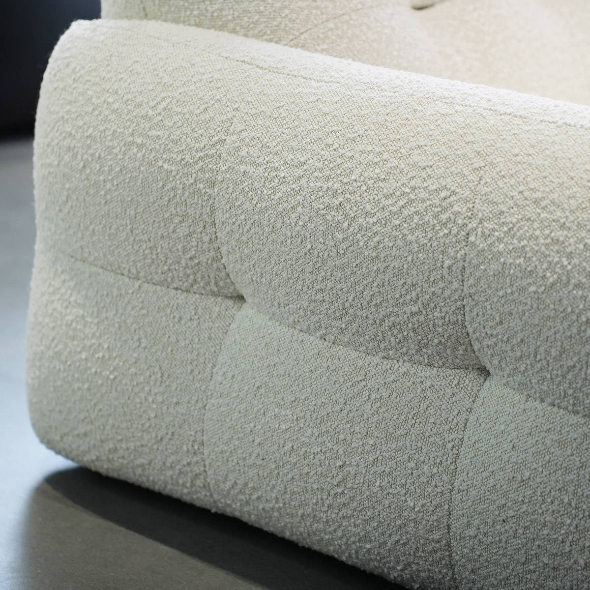 Close-up detail of the textured fabric upholstery and tufted stitching on the sofa arm.