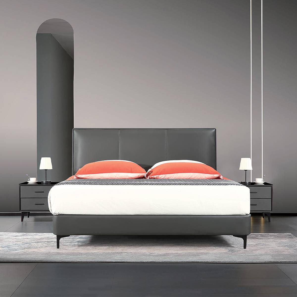 Front view of a grey upholstered bed with orange pillows and white bedding, set against a grey wall with an arched mirror.