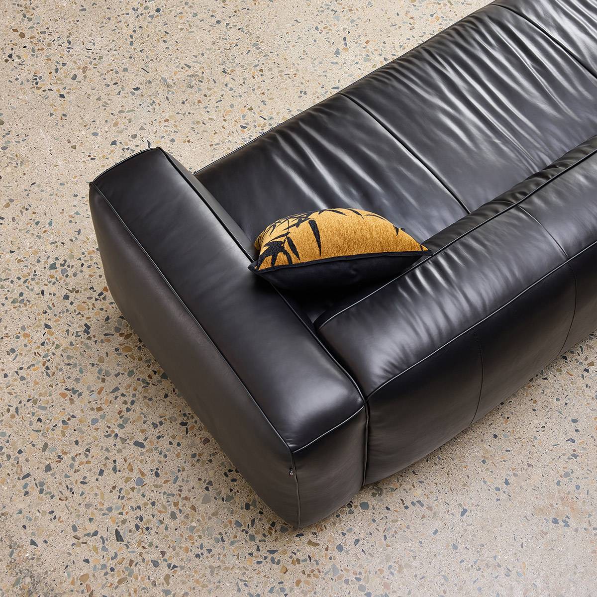 Close-up view of the black leather sofa corner showing the texture and a decorative pillow