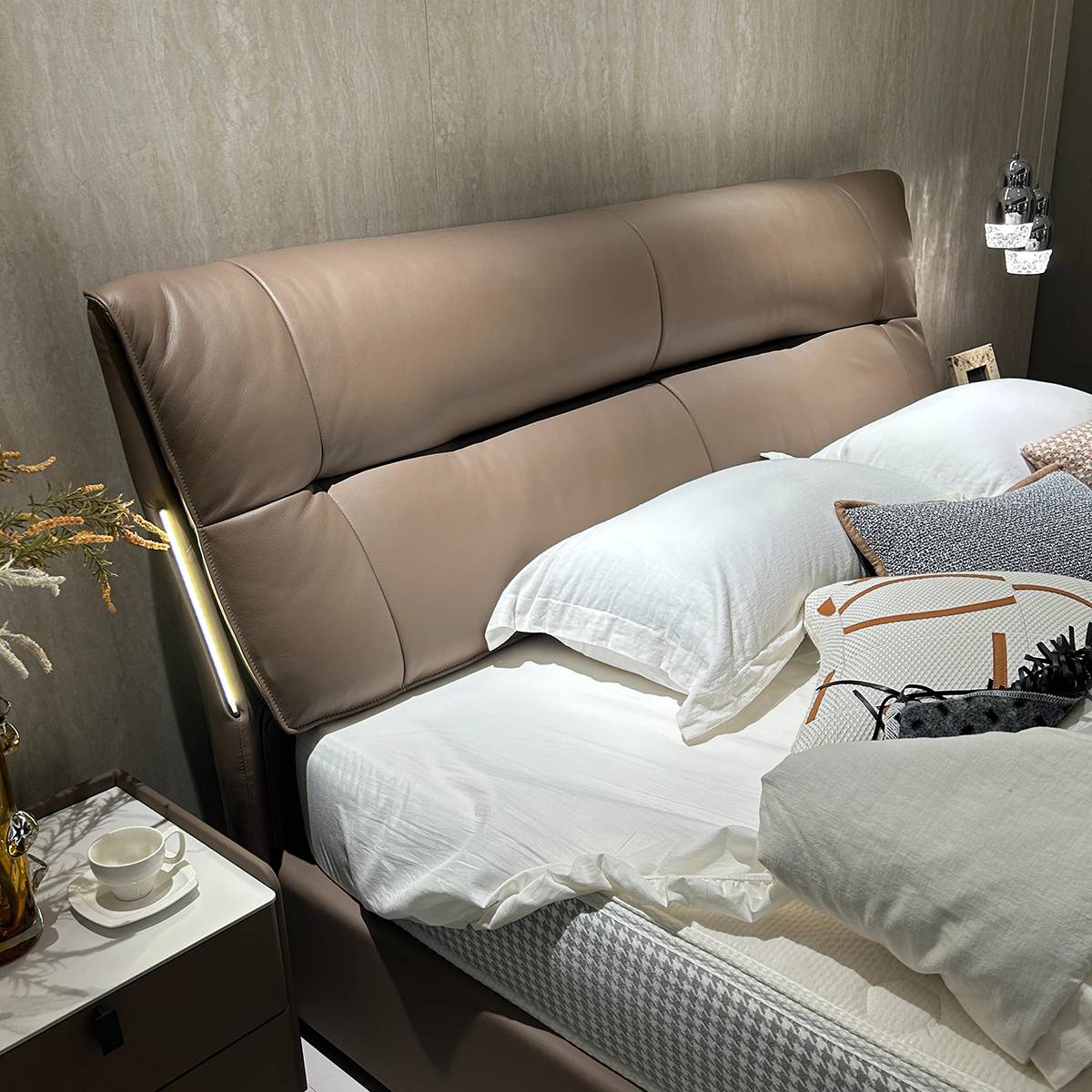 Close-up of a beige leather bed headboard with integrated lighting strip and white bedding