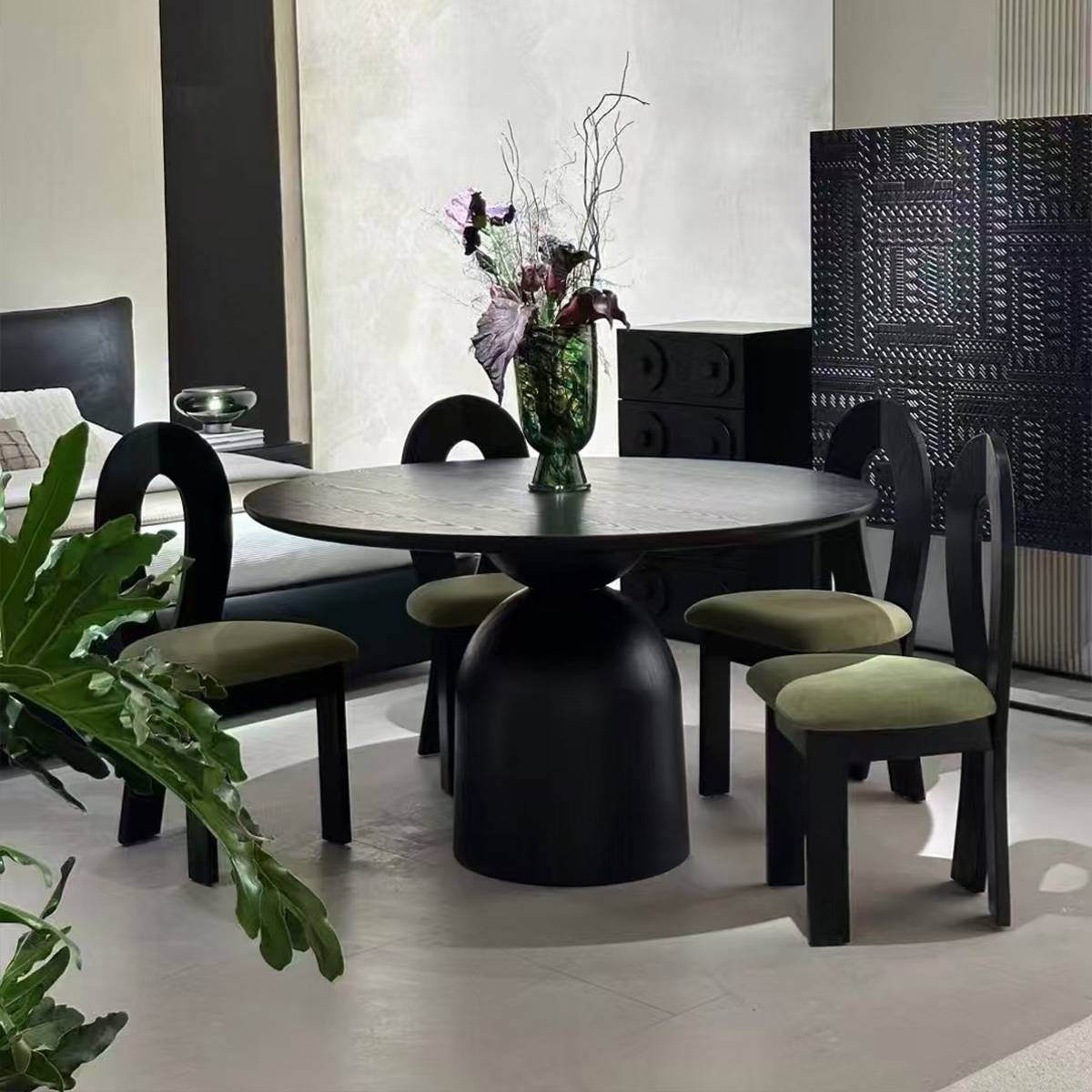 Black round dining table with a dark finish and green upholstered chairs in a modern setting.