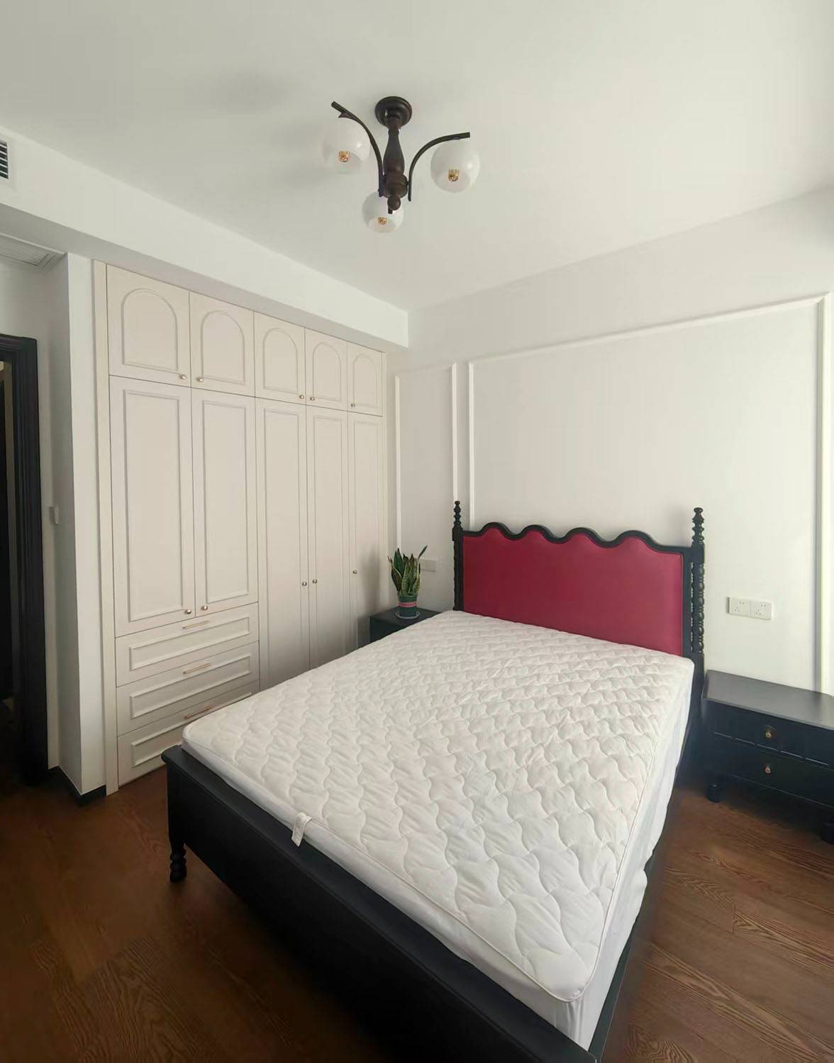 Bedroom with a black wooden bed frame, red upholstered headboard, and white wardrobe.