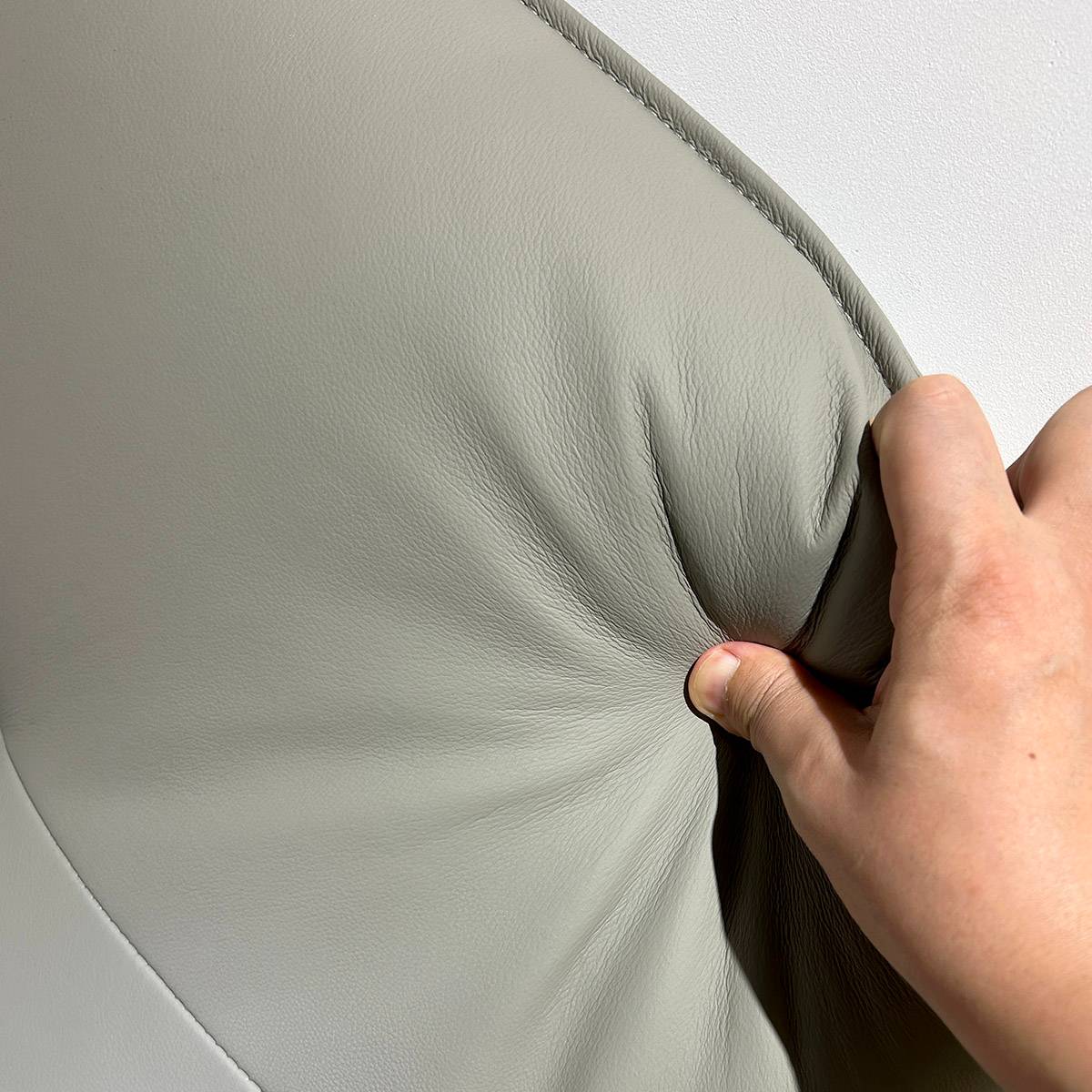 Close-up of a hand pressing into the leather headboard to demonstrate material texture and softness