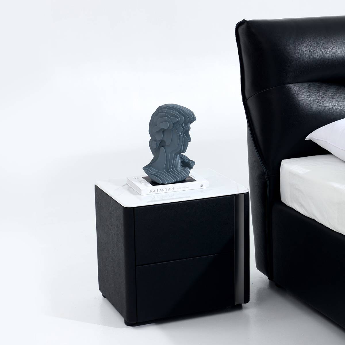 Side view of the black leather bed next to a matching bedside table with a decorative bust