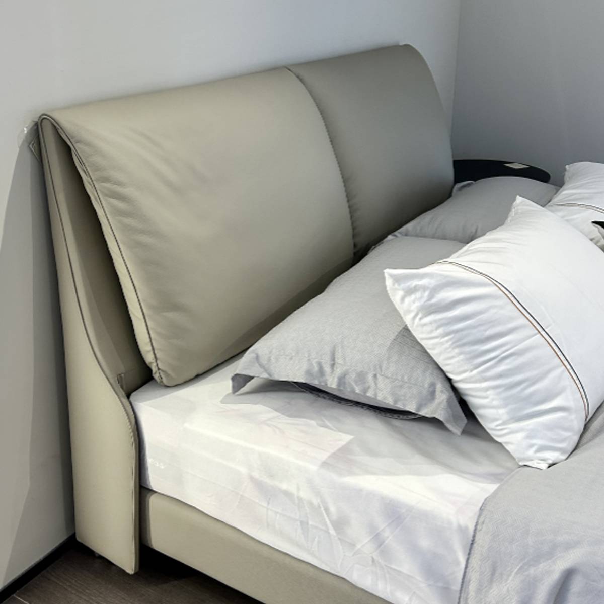 Full view of the beige leather bed with curved headboard and white bedding