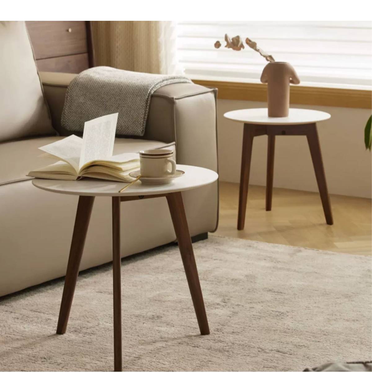 Lifestyle shot of a white round side table with walnut legs next to a sofa
