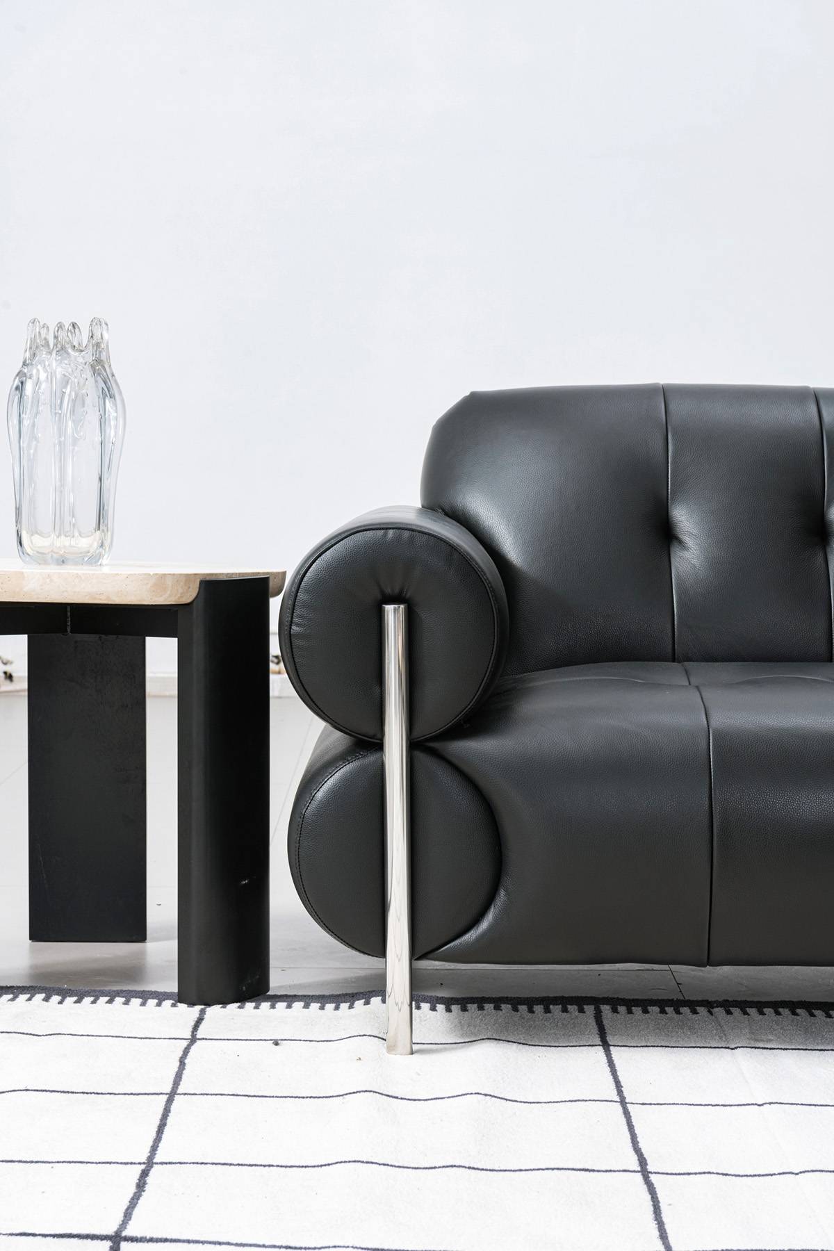 Side view of the black leather sofa armrest and stainless steel leg next to a side table.