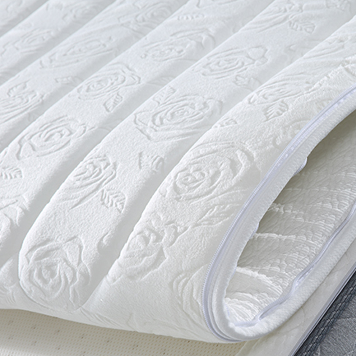 Close-up of the white mattress surface showing the embossed floral pattern and zipper detail.