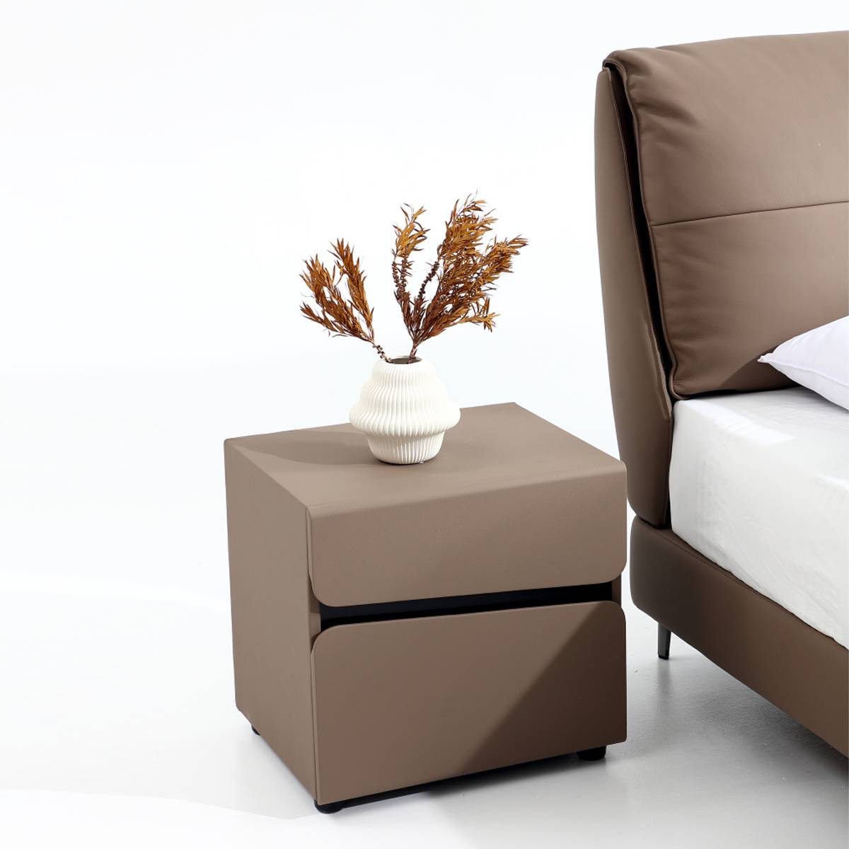 Close-up of the bedside table with a white vase and dried flowers next to the bed headboard