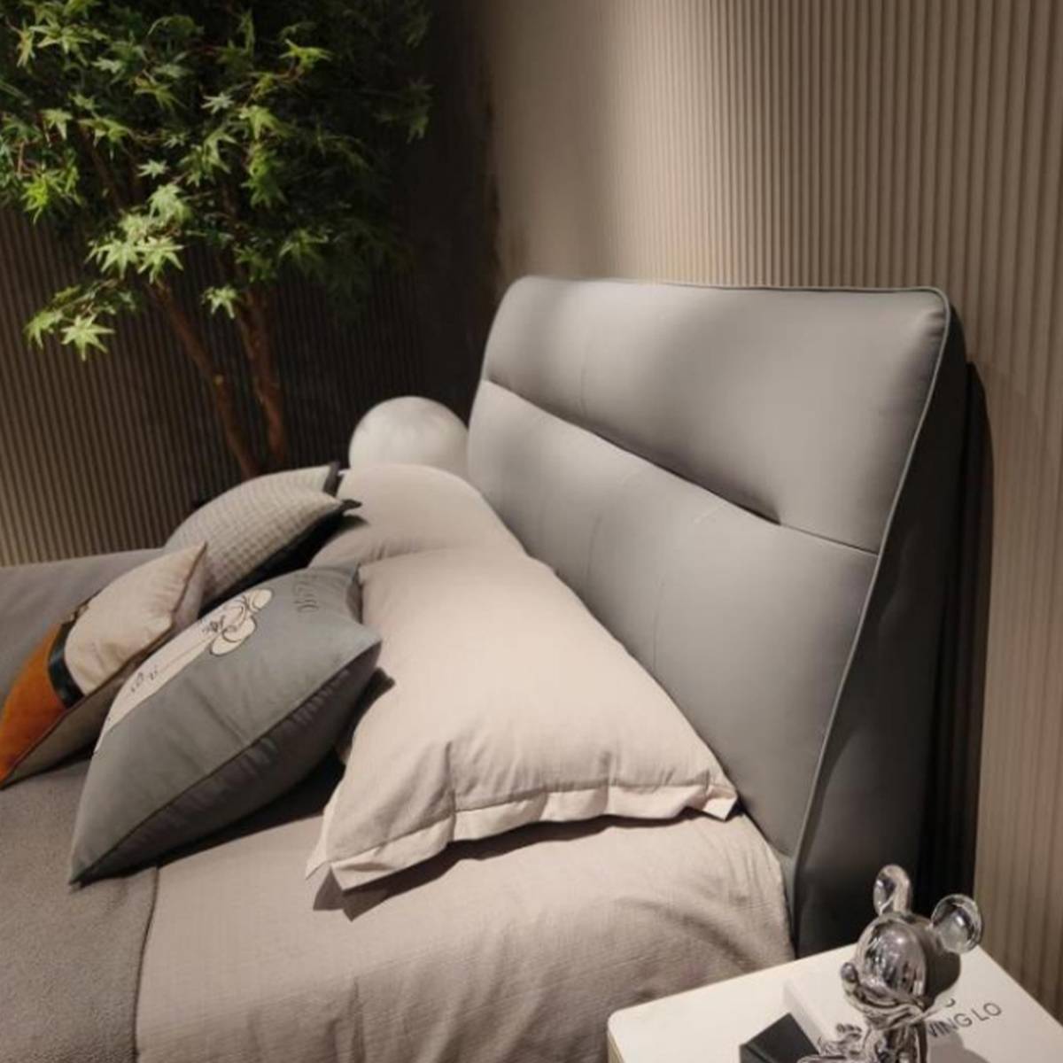 Close-up of a grey upholstered bed headboard with pillows and a bedside table
