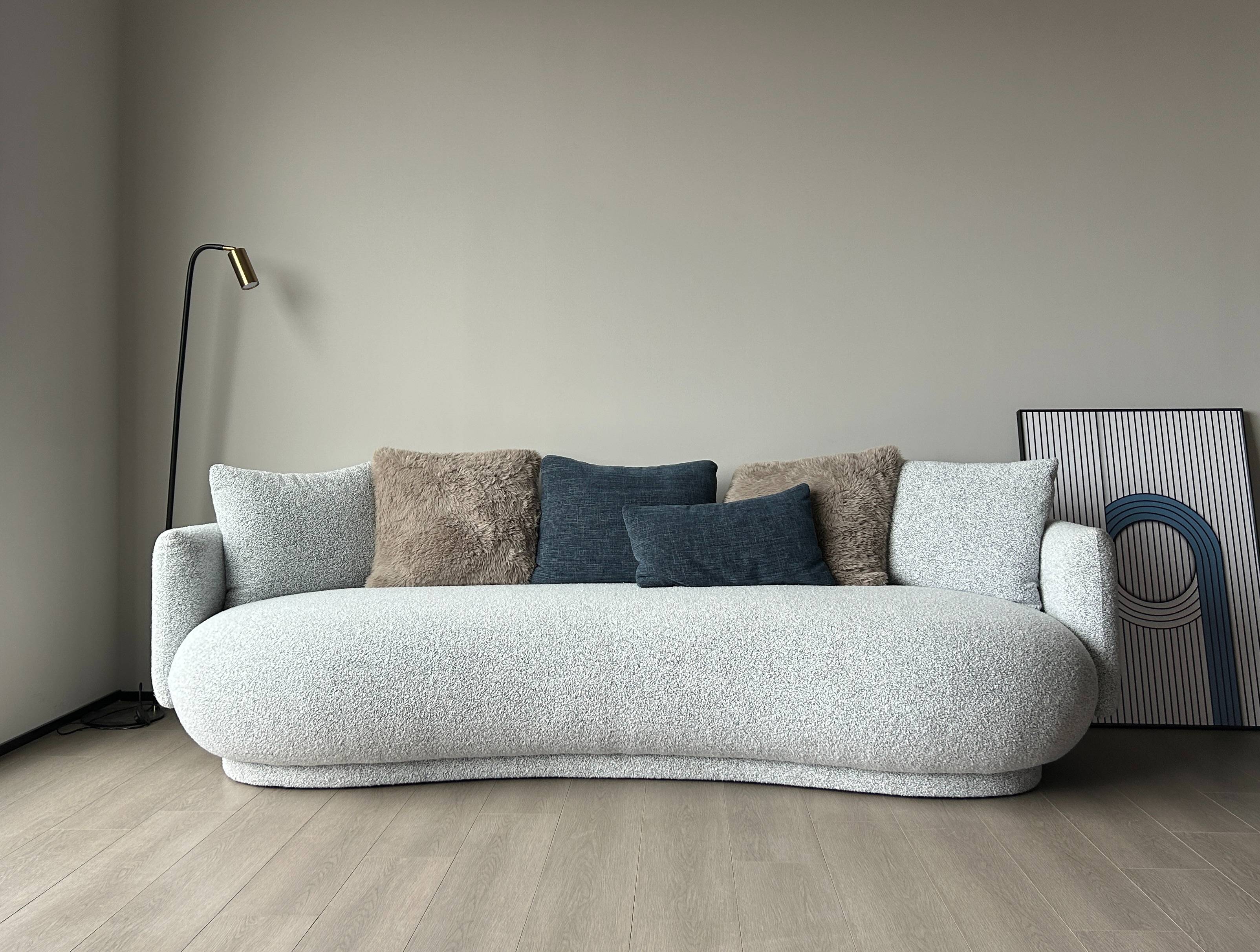 Front view of a light grey curved fabric sofa with blue and beige cushions against a plain wall.
