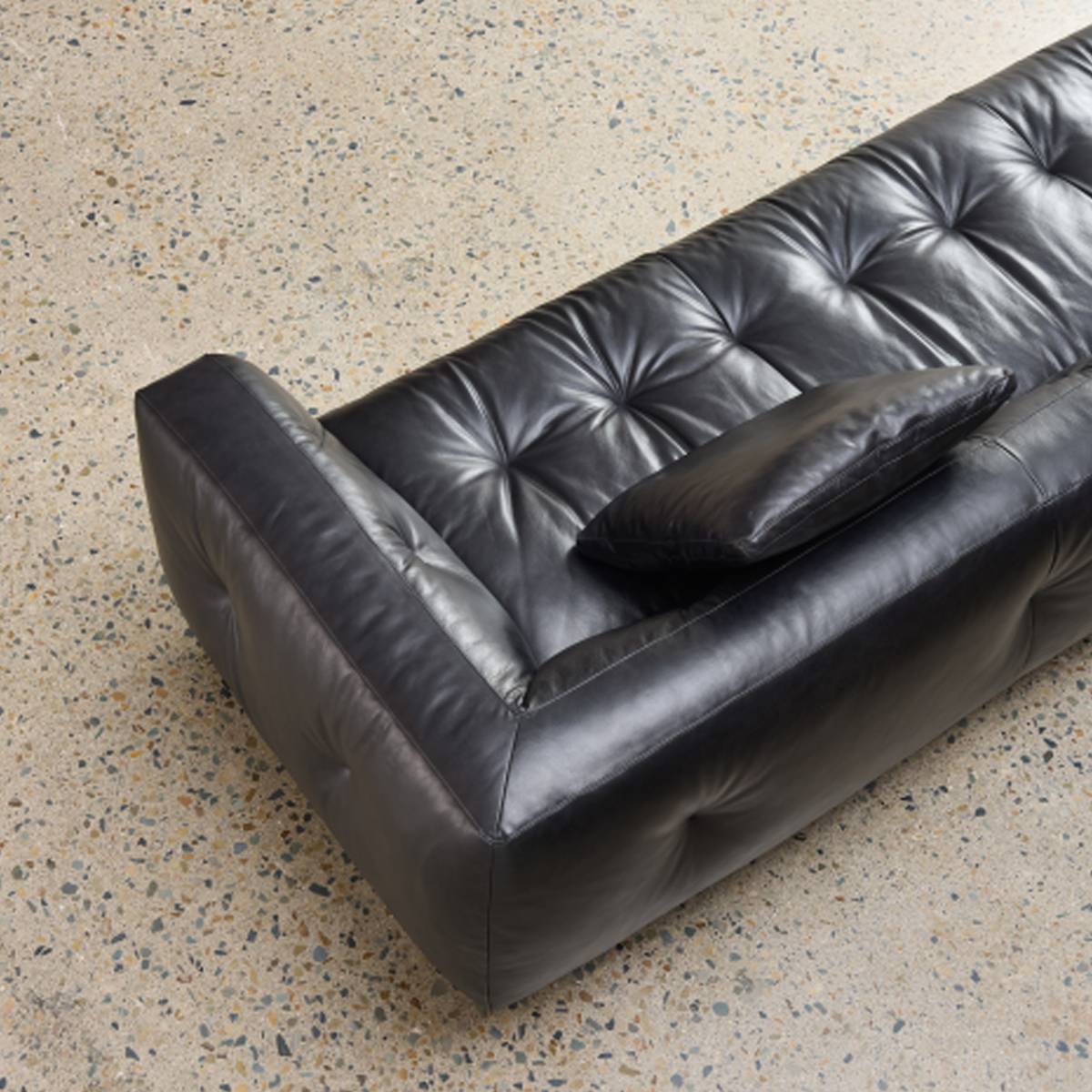 High-angle view of the black leather sofa corner showing the armrest and down cushion