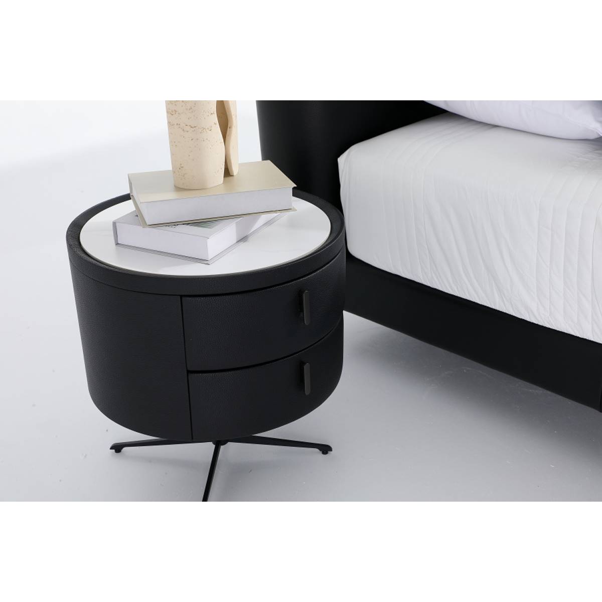 Side view of the black upholstered bed frame next to a matching round bedside table