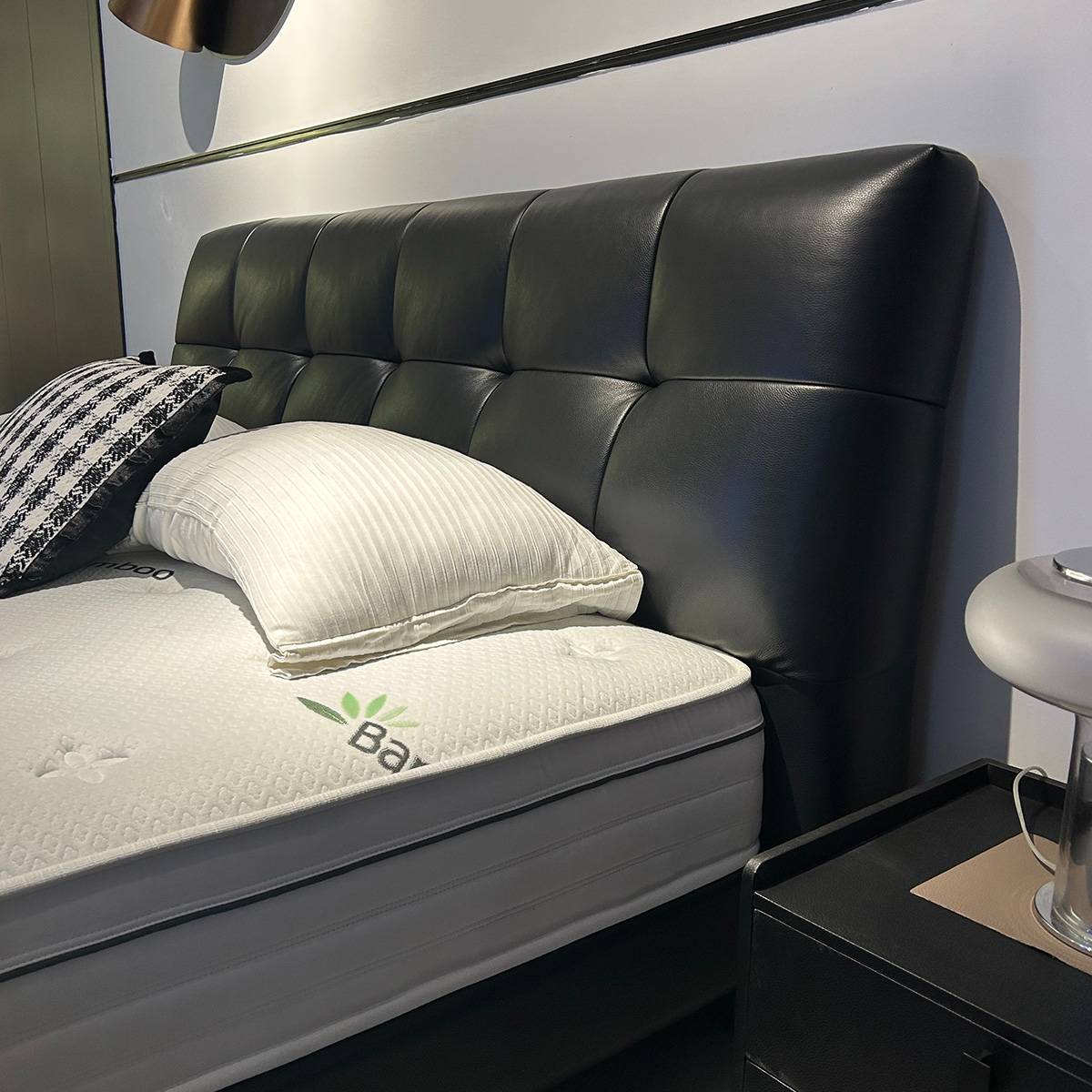 Front view of the black leather tufted bed with white bedding and bedside tables.