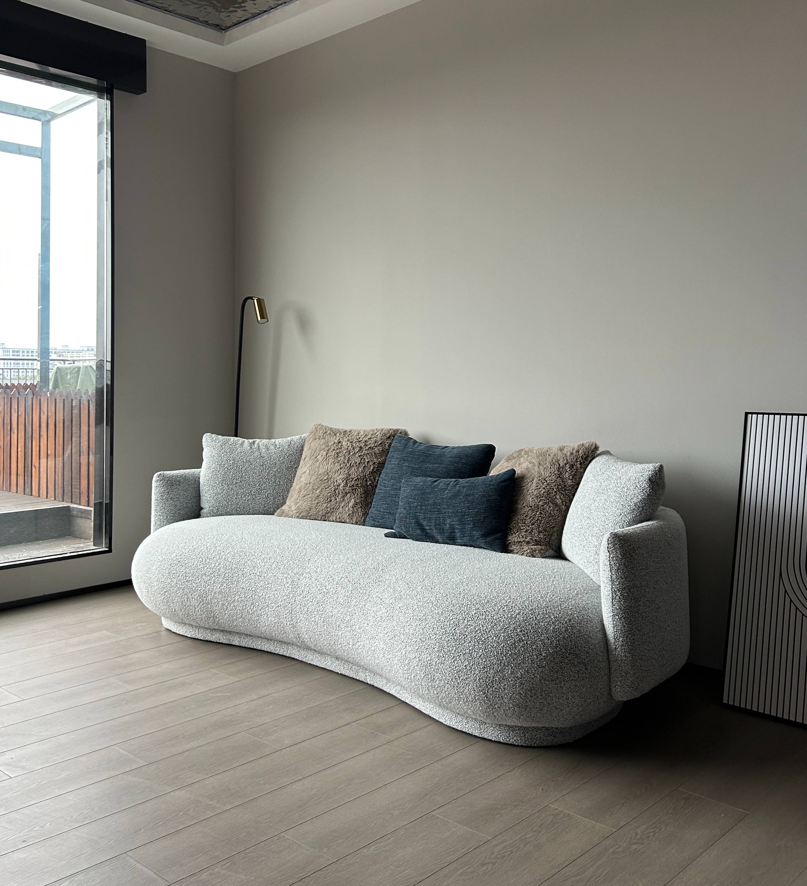 Side angle view of the curved sofa in a living room setting with a large window.
