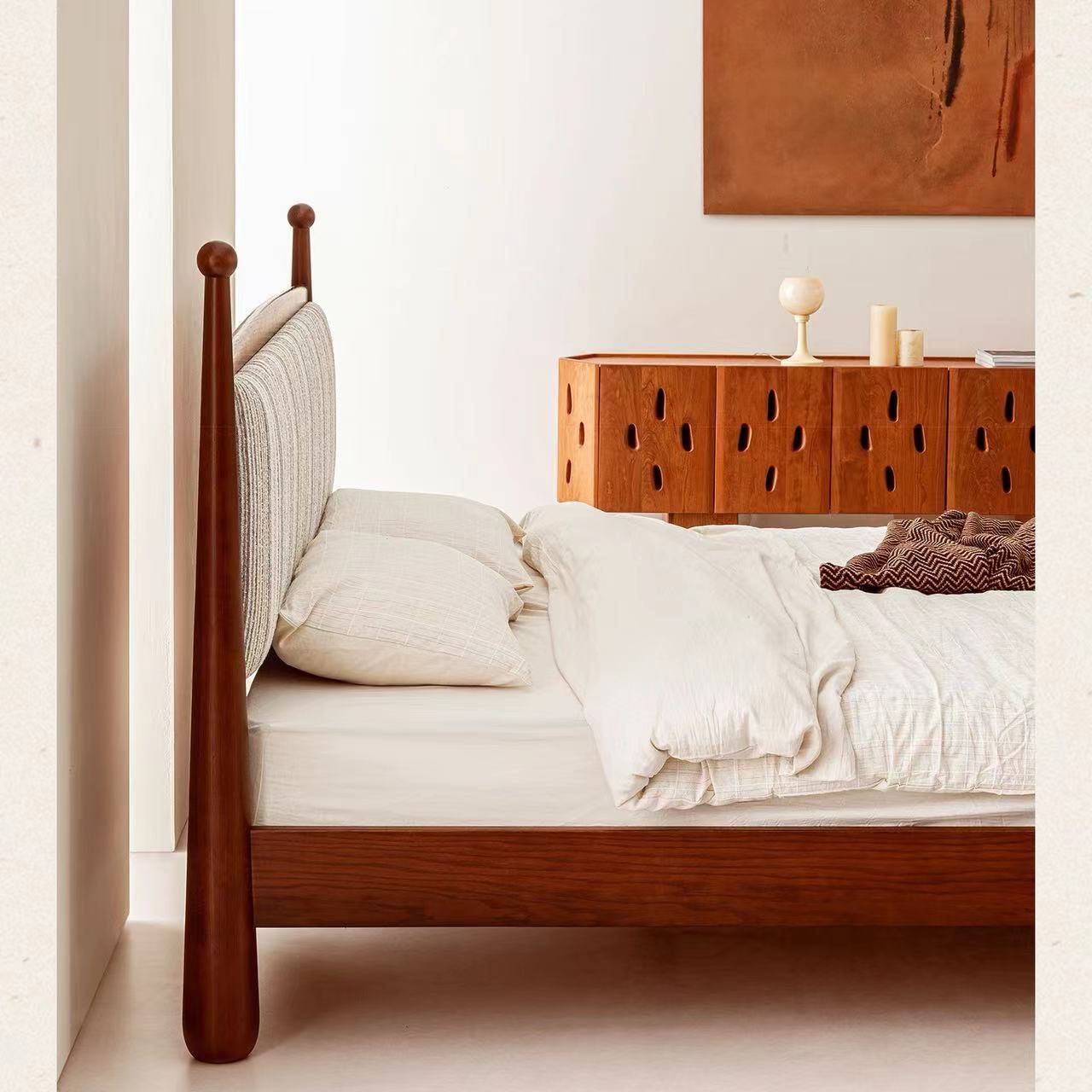 Side view of a mid-century solid wood bed with a fabric headboard and white bedding
